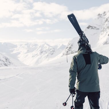 Skifahrer in olivgrüner Jacke steht auf präparierter Piste und trägt Skier auf der Schulter, Blick auf ein weites verschneites Tal, das Valzifenztal in Gargellen im Montafon.  | © Gargellner Bergbahnen GmbH & Co KG, Daniel Zangerl