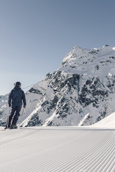 Ein Skifahrer steht auf einer frisch präparierten Piste in Gargellen mit Blick auf verschneite Berge und Sessellift. | © Gargellner Bergbahnen, Daniel Zangerl