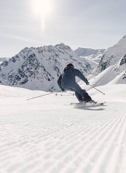 Skifahrer fährt in Schwüngen eine frisch präparierte Piste in Gargellen hinunter, verschneite Bergkulisse im Hintergrund. | © Gargellner Bergbahnen GmbH & Co KG, Daniel Zangerl