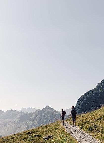 Zwei Wanderer gehen auf einem Bergpfad in Gargellen, umgeben von grünen Hängen und Felsmassiven. | © Gargellner Bergbahnen GmbH & Co KG, Daniel Zangerl
