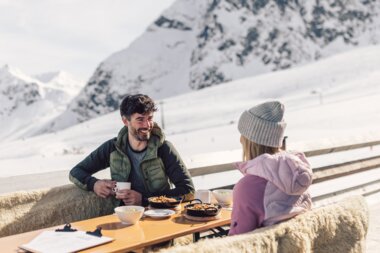 Ein Mann und eine Frau sitzen an einem Tisch auf der Terrasse eines Bergrestaurants und genießen jeweils ein Essen und ein warmes Getränk.  | © Gargellner Bergbahnen GmbH & Co KG, Daniel Zangerl